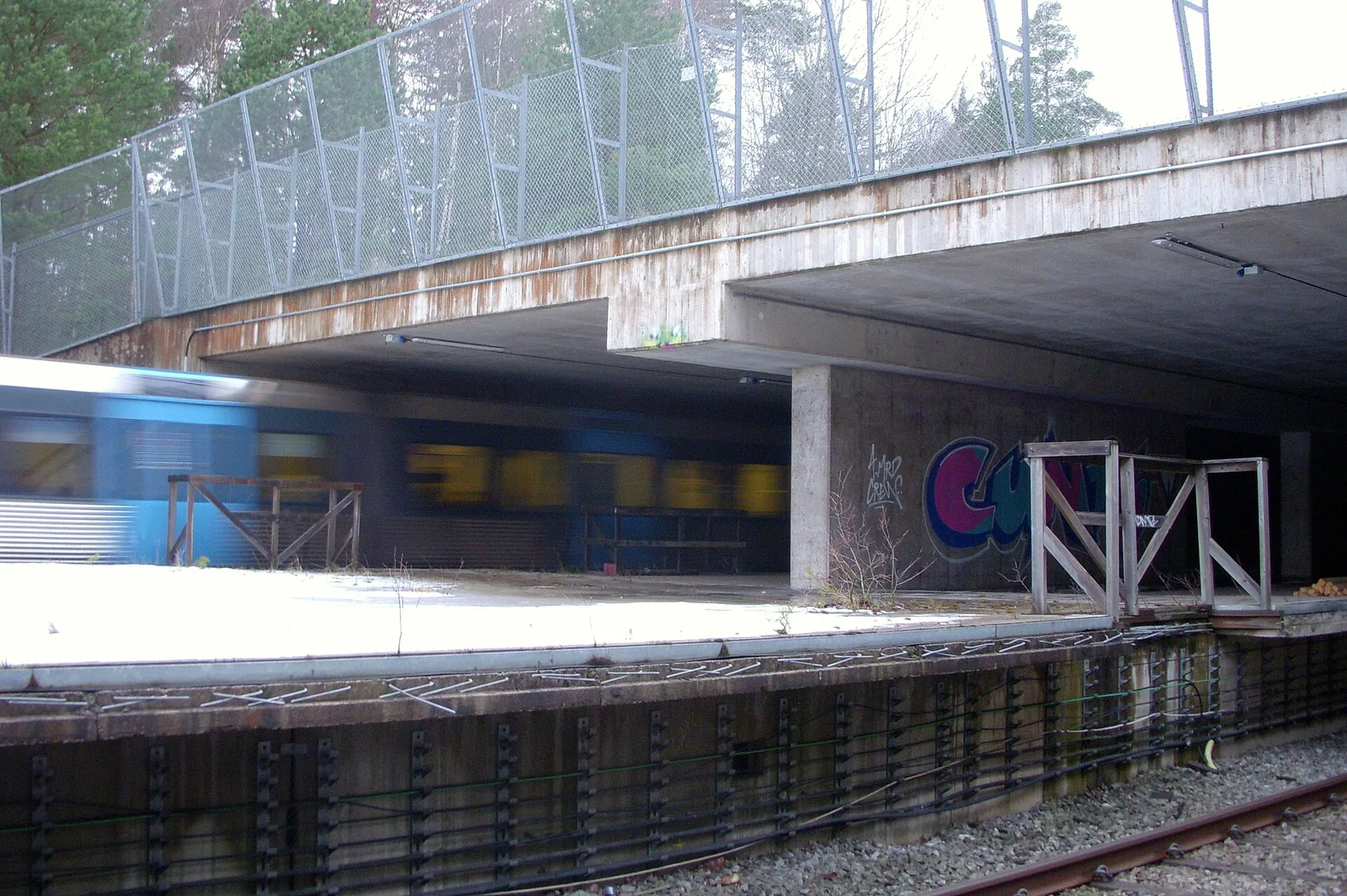 The abandoned Kymlinge ghost subway station with a train passing through, graffiti on the concrete platform