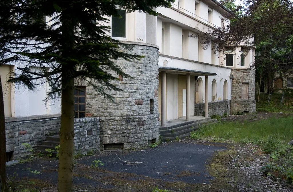 The abandoned Taunus-Sanatorium Dr. Goldschmidt in Bad Homburg: an empty rendered building with a round stone stair tower and bricked-up entrance loggia, overgrown by trees