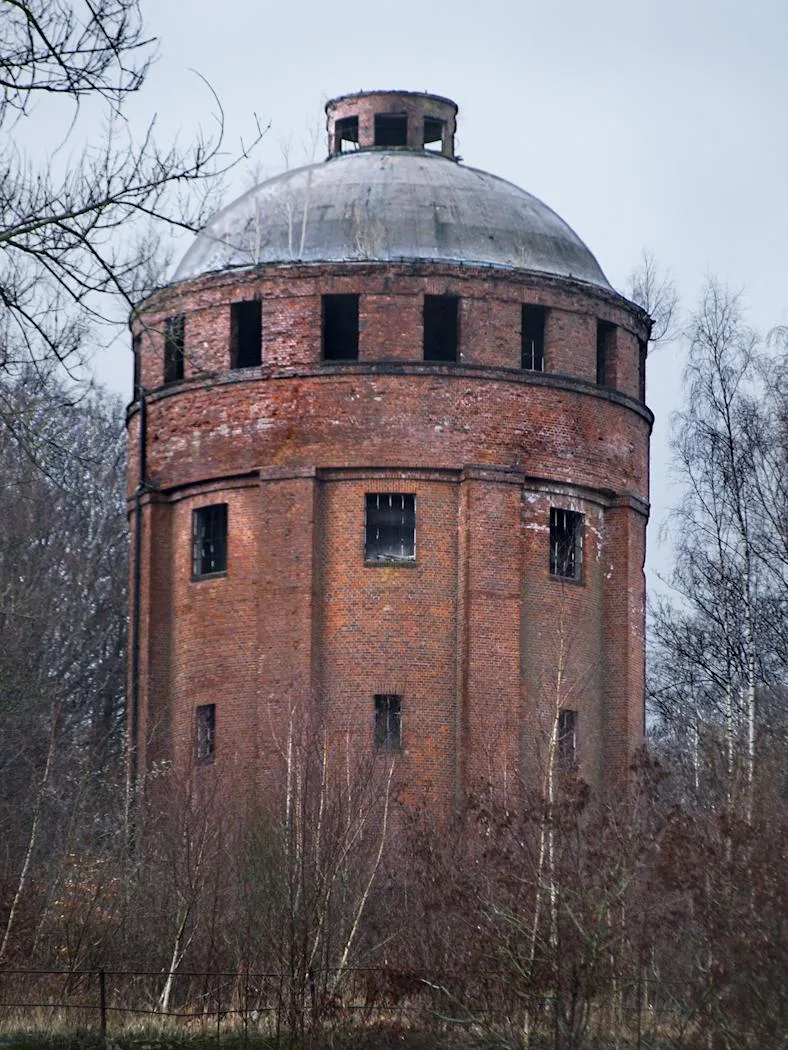 Der von Bäumen halb verdeckte, eingezäunte Wasserturm der ehemaligen Dynamitfabrik Krümmel bei Geesthacht