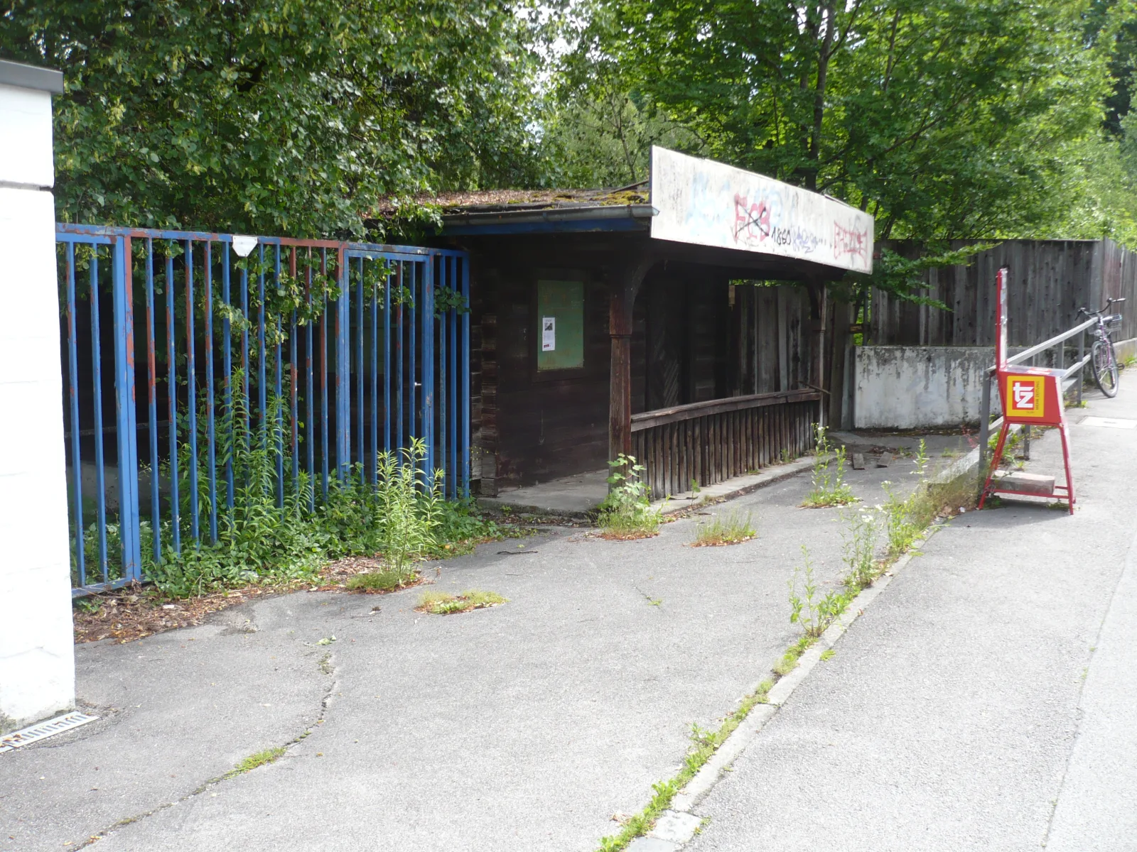Decaying wooden ticket kiosk and entrance area of the abandoned Familienbad Floriansmühle in Munich-Freimann, overgrown and covered in graffiti