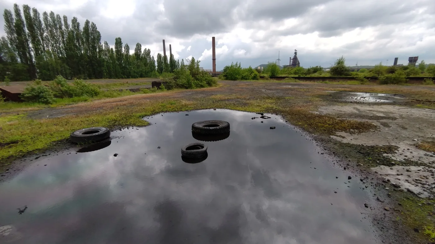 Friche post-industrielle au pied des terrils de Charleroi, avec cheminées d'usine à l'horizon