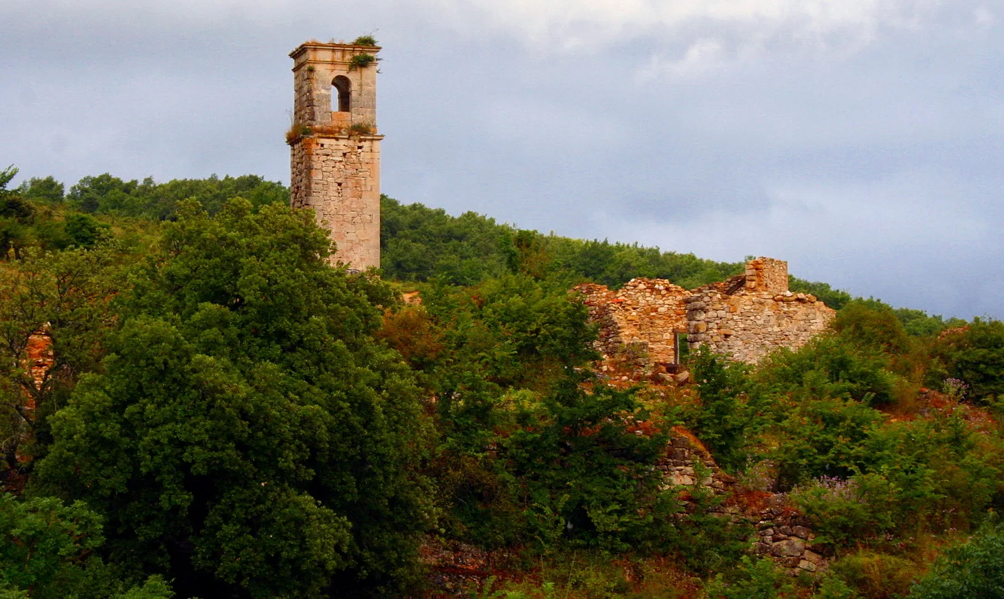Ruinas de Ochate con la torre de la iglesia románica de San Miguel sobre una ladera arbolada