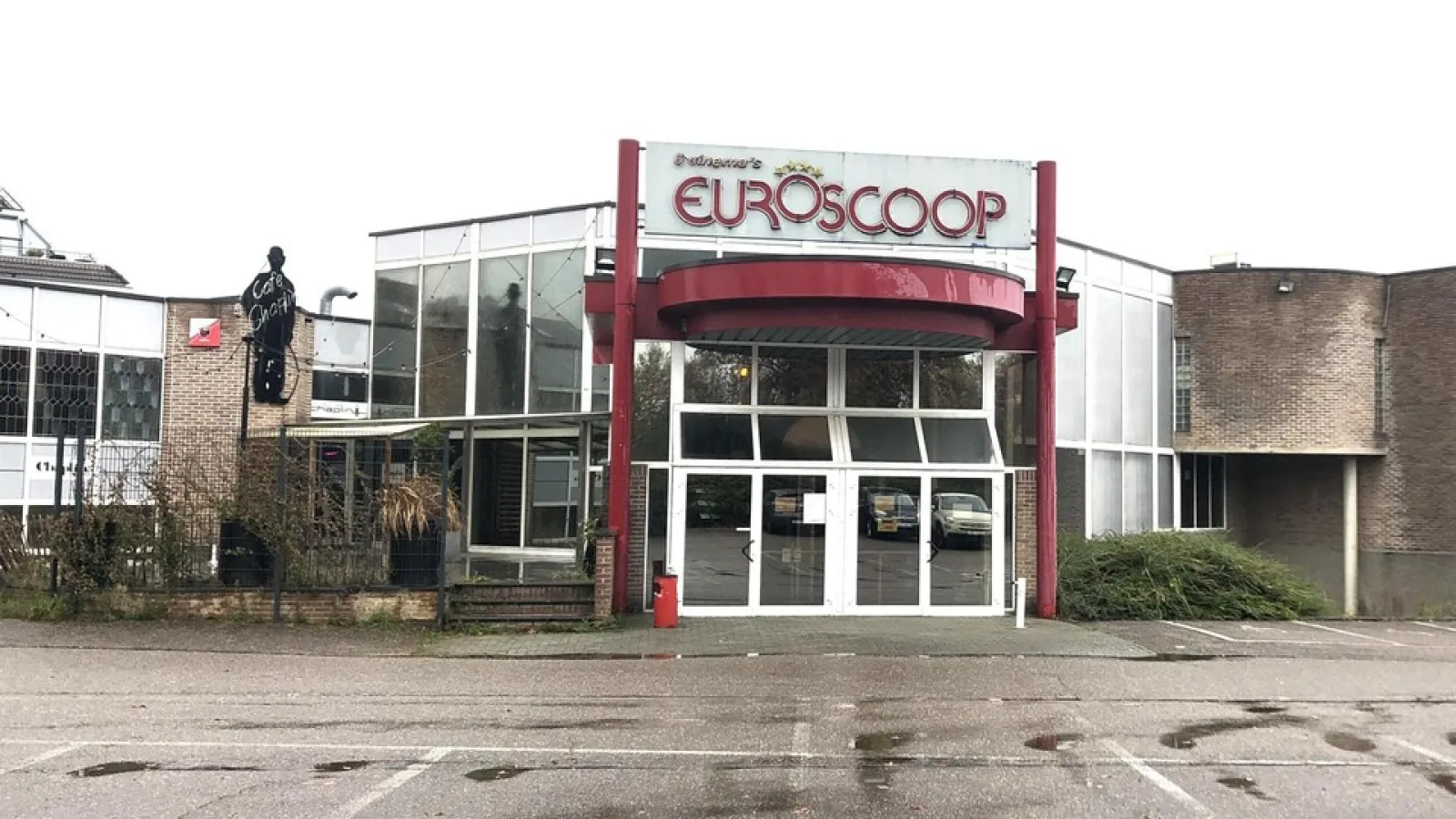 Verlaten ingang van het Euroscoop-bioscoopcomplex in Lanaken, met de Euroscoop-lichtreclame boven de glazen entree en een leeg parkeerterrein