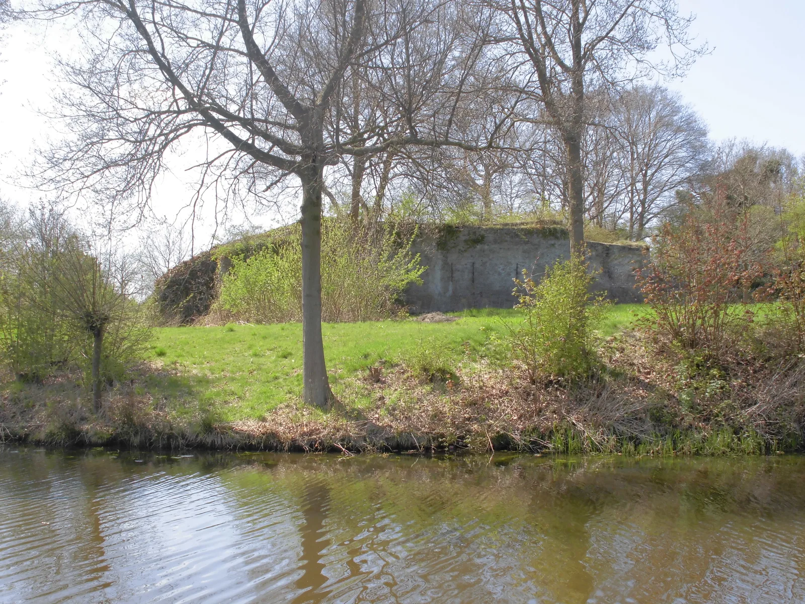Het overwoekerde aardwerk en de mossige bakstenen muur van het Fort bij Tienhoven achter de gracht