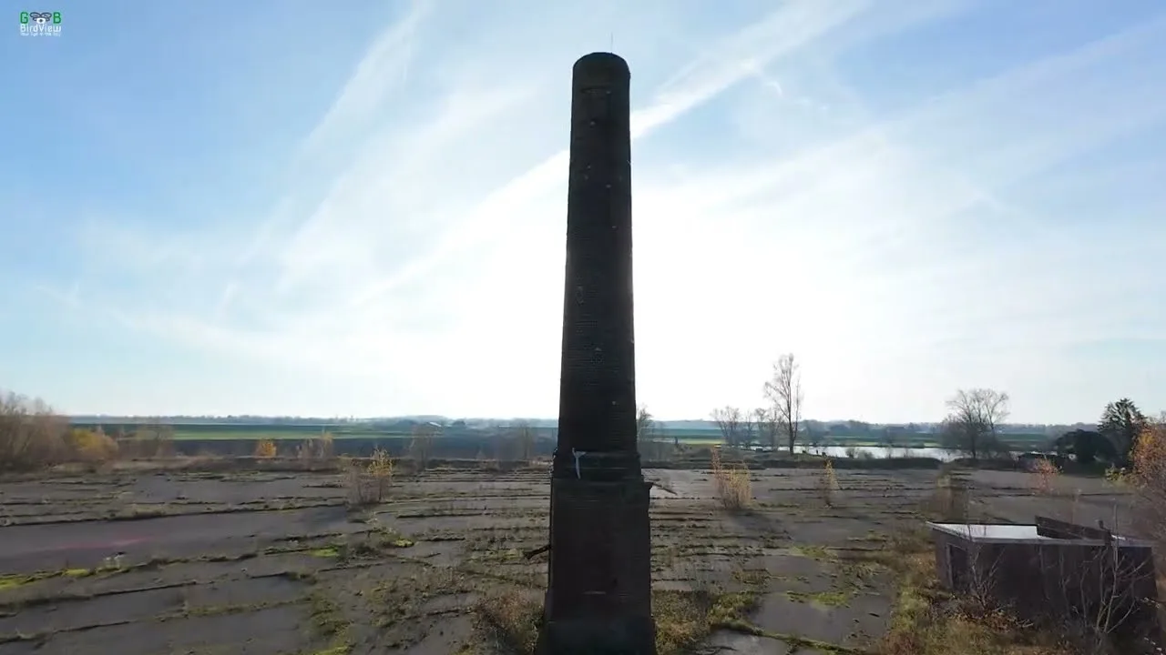 De hoge bakstenen schoorsteen van de verlaten steenfabriek De Roodvoet boven het vervallen terrein aan de Lek